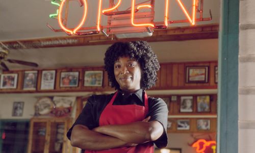 Texas restaurant owner standing with neon open sign in the window