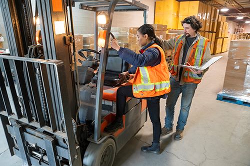 Two students inspecting a forklift wearing orange safety vests